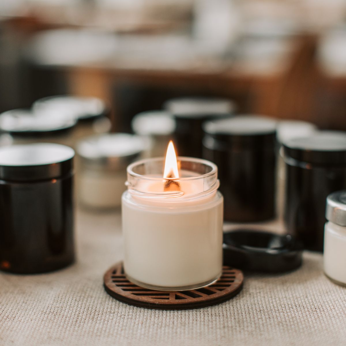 Lit cream candle in a glass jar on a wooden trivet, amber jars behind
